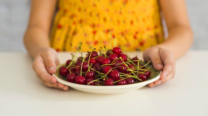 Una niña sostiene un plato de cerezas. 