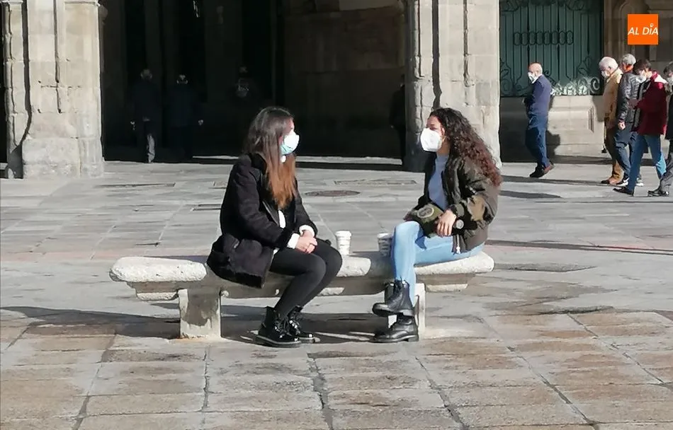 Dos jóvenes conversan en un banco de la Plaza Mayor mientras toman un café. Fotos: Lydia González