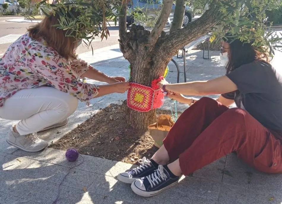 Dos de las participantes del taller de ganchillo colocando los bordados en uno de los árboles de Villares de la Reina