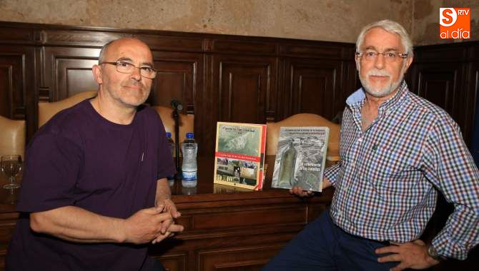 Dos de los ponentes muestran el libro sobre el que se basaba la conferencia