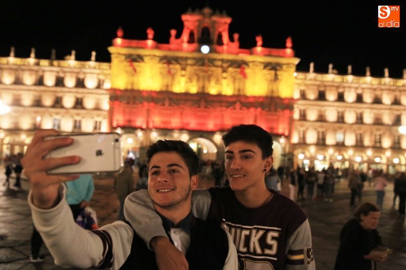 Unos jóvenes se hacen una foto con la fachada iluminada detrás