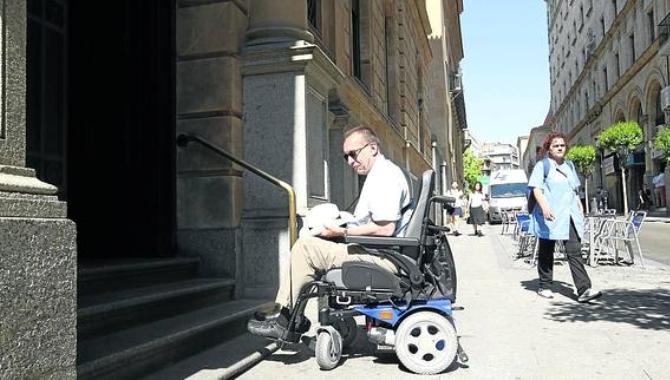 Un hombre en silla de rueda junto a las escaleras de la delegación de Hacienda